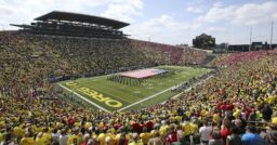 Autzen stadium filled with people and band on field with large flag